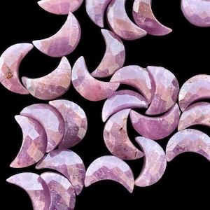 May include: A collection of pale pink, faceted, crescent moon shaped gemstone beads. The beads are arranged in a random pattern on a black background.