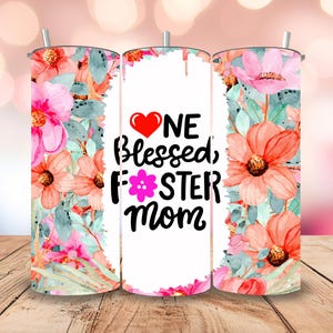 May include: A white tumbler with a floral design and the text "One Blessed Foster Mom" with a pink flower and a red heart.