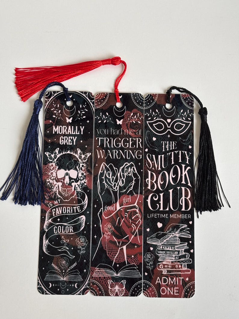 May include: Set of three black and red bookmarks with a skull, hands, and a mask. The bookmarks have white text that reads "Morally Grey is my favorite color", "You had me at Trigger Warning", and "The Smutty Book Club Lifetime Member Admit One".