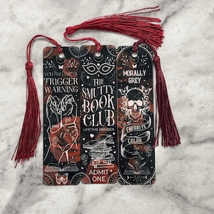May include: Three bookmarks with red tassels. The bookmarks feature a black and red background with white text and illustrations. The text on the bookmarks reads "You had me at trigger warning", "The Smutty Book Club", and "Morally Grey is my favorite color".
