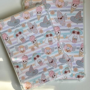 May include: Two clear tablet cases featuring a repeating pattern of pastel-colored ghosts wearing hats, winged candy corn, ice cream cones with skull tops, and small flowers over a background of horizontal stripes in shades of pink, blue, and orange.