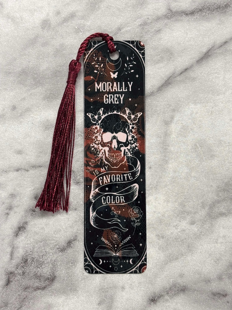 May include: A black and red bookmark with a skull and the text "Morally Grey is my favorite color". The bookmark has a red tassel.