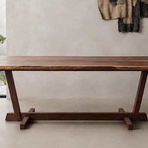 May include: A rectangular dining table crafted from dark brown wood with a natural live edge along the long sides. The table features a sturdy base with two angled support legs connected by a horizontal stretcher bar resting on the floor.