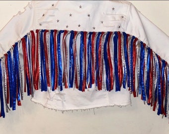 May include: White denim jacket with red, white, and blue fringe trim. The jacket has a distressed look with small silver stars.