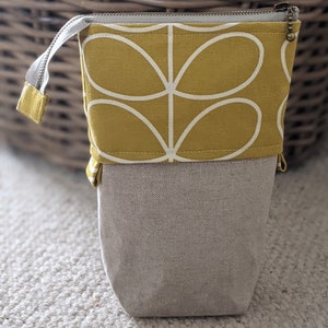Puede incluir: Un estuche para l&aacute;pices de tela amarilla con un dise&ntilde;o floral estilizado blanco. El estuche tiene una cremallera y un forro de tela beige.