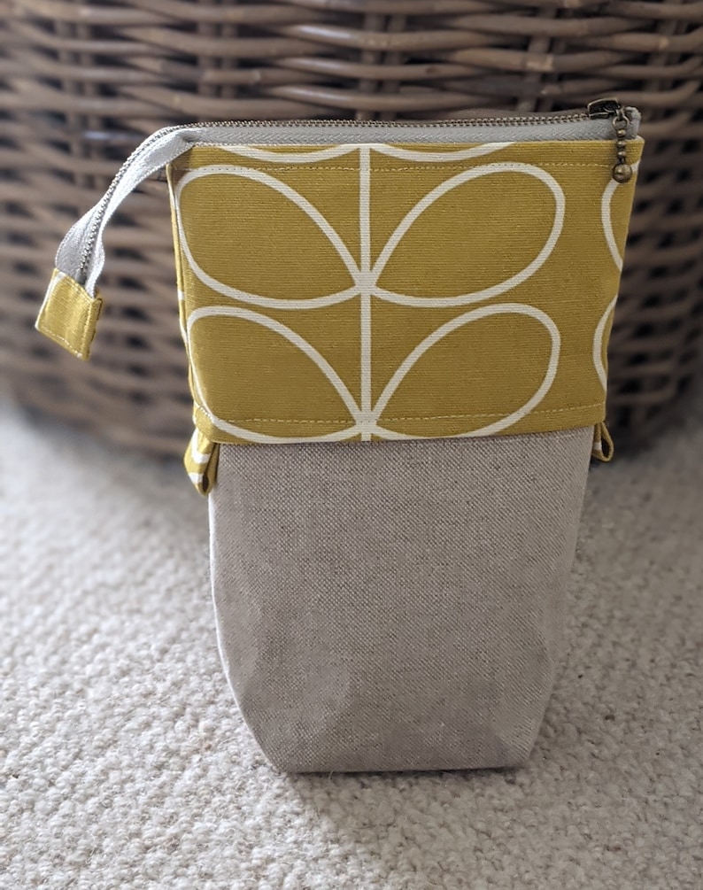 Puede incluir: Un estuche para l&aacute;pices de tela amarilla con un dise&ntilde;o floral estilizado blanco. El estuche tiene una cremallera y un forro de tela beige.