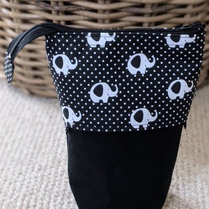 Peut inclure: Une trousse à crayons noire et blanche avec une fermeture à glissière. La trousse est décorée d'un motif répété d'éléphants blancs sur un fond noir avec des pois blancs.