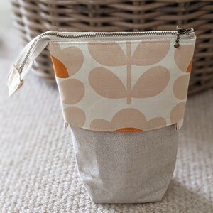 Puede incluir: Una bolsa de cremallera beige con un patr&oacute;n floral en naranja y beige. La bolsa est&aacute; hecha de tela y tiene una textura similar al lino.
