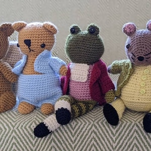 May include: Four crocheted stuffed animals, a brown kangaroo, a brown bear wearing a blue shirt, a green frog wearing a pink and red jacket, and a purple mouse wearing a green jacket.