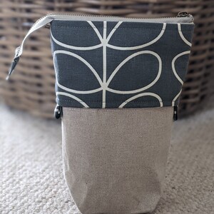Puede incluir: Una bolsa con cremallera gris y beige con un dise&ntilde;o floral estilizado blanco. La bolsa est&aacute; hecha de tela y tiene un cierre de cremallera.