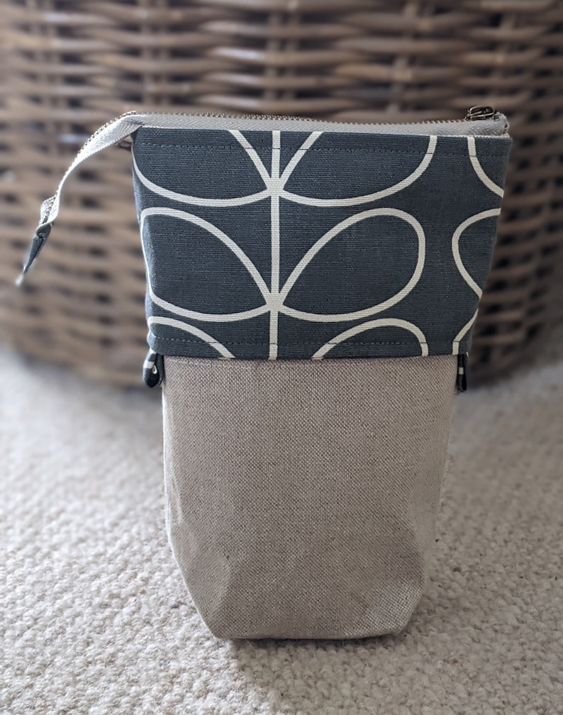 Puede incluir: Una bolsa con cremallera gris y beige con un dise&ntilde;o floral estilizado blanco. La bolsa est&aacute; hecha de tela y tiene un cierre de cremallera.