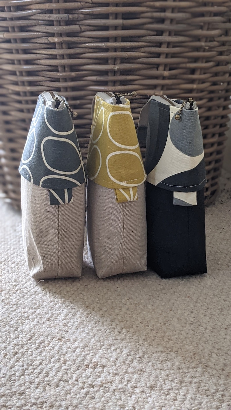 Puede incluir: Tres bolsas con cremallera con diferentes patrones de tela. Las bolsas est&aacute;n hechas de tela de lino natural y tienen un patr&oacute;n geom&eacute;trico negro, gris y amarillo.