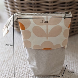 Puede incluir: Una bolsa con cremallera de estampado floral beige y naranja con base de tejido de lino. La bolsa mide 8 cm de ancho, 6 cm de alto y 15 cm de largo.