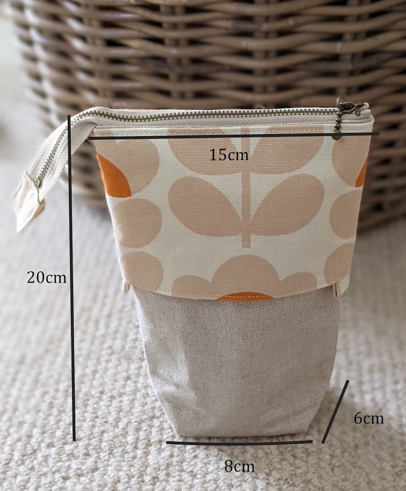 Puede incluir: Una bolsa con cremallera de estampado floral beige y naranja con base de tejido de lino. La bolsa mide 8 cm de ancho, 6 cm de alto y 15 cm de largo.