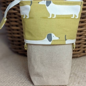 Könnte beinhalten: Eine gelbe Stiftetui aus Canvas mit einem weißen Reißverschluss und einem Muster aus weißen Dackeln auf gelbem Hintergrund. Die Etui ist aus robustem Canvas-Material gefertigt und hat einen Reißverschluss.