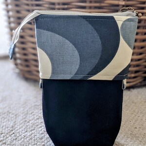 Puede incluir: Una bolsa con cremallera negra y blanca con un patr&oacute;n geom&eacute;trico. La bolsa tiene un forro de tela negro.