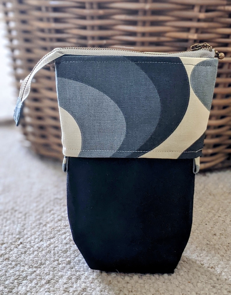 Puede incluir: Una bolsa con cremallera negra y blanca con un patr&oacute;n geom&eacute;trico. La bolsa tiene un forro de tela negro.