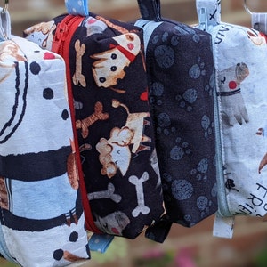May include: Five zippered pouches with different dog-themed patterns. The pouches are made of fabric and have a zipper closure. The patterns include paw prints, bones, and dogs.