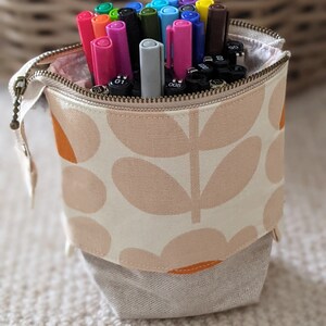 Puede incluir: Un estuche de l&aacute;pices de tela blanca con un patr&oacute;n floral en naranja y rosa. El estuche est&aacute; lleno de marcadores de varios colores.