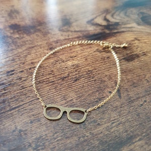 May include: A gold chain necklace with a pair of glasses pendant.