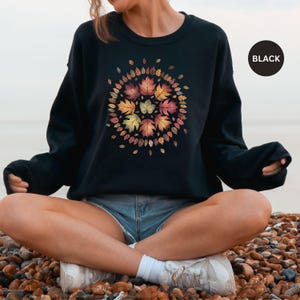 May include: A black sweatshirt with a colorful autumn leaf design. The leaves are arranged in a circle and are in shades of red, orange, yellow, and brown.