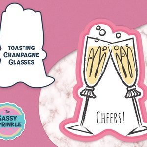 Może przedstawiać: Naklejka przedstawiająca dwa kieliszki szampana stukające się, wypełnione żółtym płynem i bąbelkami. Słowo "Cheers!" jest napisane pod kieliszkami. Naklejka ma różową obwódkę na różowym tle. Obecny jest również tekst "Toasting Champagne Glasses".