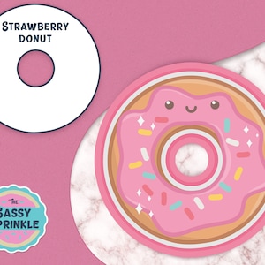 May include: A pink and brown donut with a smiling face and sprinkles. The donut has the text "STRAWBERRY DONUT" on a white circle above it. The text "The Sassy Sprinkle" is on a blue circle with a pink background.
