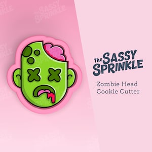 Puede incluir: Cortador de galletas de cabeza de zombie verde con cerebro rosa y sangre goteando. El cortador de galletas está sobre un fondo rosa con el texto "The SASSY SPRINKLE" y "Zombie Head Cookie Cutter".