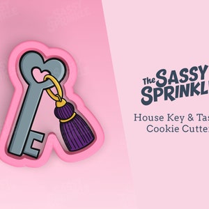 Op de afbeelding: Een roze plastic koekjesvormpje in de vorm van een huissleutel met een paarse kwast. Het koekjesvormpje is op een roze achtergrond. De tekst "The Sassy Sprinkle" en "House Key & Tassel Cookie Cutter" staat op de achtergrond.