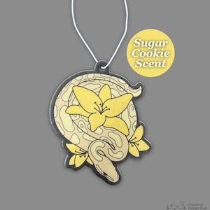 May include: A car air freshener shaped like a snake with yellow flowers. The air freshener is labeled "Sugar Cookie Scent".