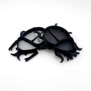 May include: Black plastic scarab beetle cookie cutters. The cutters are in the shape of a beetle with detailed legs and body segments. The cutters are designed for baking and crafting.