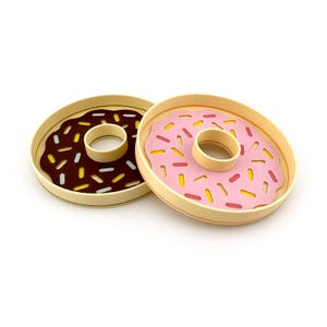 May include: Two wooden donut-shaped serving trays, one with pink frosting and yellow sprinkles, the other with brown frosting and white and yellow sprinkles.