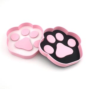 May include: Two pink paw-shaped containers with black interiors. The containers are open and show the paw print design inside.