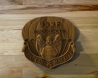 May include: A wooden plaque with a carved image of a parachute, an angel holding a globe, and the text "USAF PARARESCUE THAT OTHERS MAY LIVE".