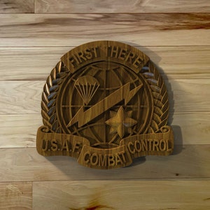 May include: A wooden plaque with the words "First There" and "U.S.A.F. Combat Control" in a banner. The plaque features a globe with a lightning bolt, a star, and a parachute.
