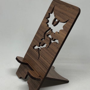 May include: A wooden phone stand with a dragon design cut out. The stand is brown and has a natural wood finish.