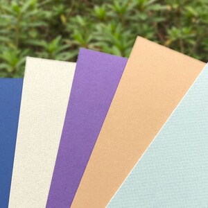 May include: Six different colored cardstock paper samples. The colors are black, blue, white, purple, beige, and light blue.