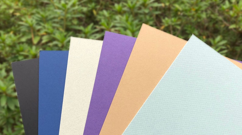 May include: Six different colored cardstock paper samples. The colors are black, blue, white, purple, beige, and light blue.