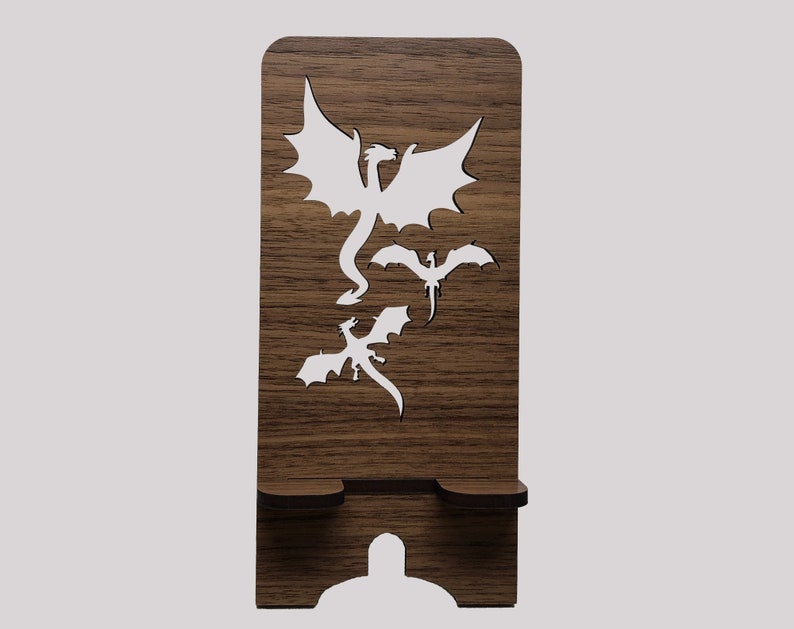 May include: A wooden phone stand with a cutout design of three dragons. The stand is brown and the dragons are white.