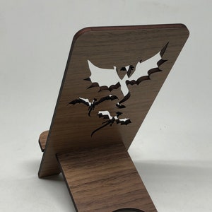 May include: A wooden phone stand with a dragon design cut out. The stand is brown with a dark brown trim. The stand is folded up and ready to use.