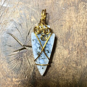 May include: A blue and white agate arrowhead pendant wrapped in gold wire with a decorative swirl design.