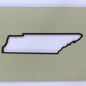 May include: A light green wooden plaque with a cutout of the state of Tennessee. The cutout is black and the plaque has a textured surface.