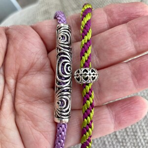 May include: Two braided cords with decorative metal beads. One cord is purple and the other is green and purple.