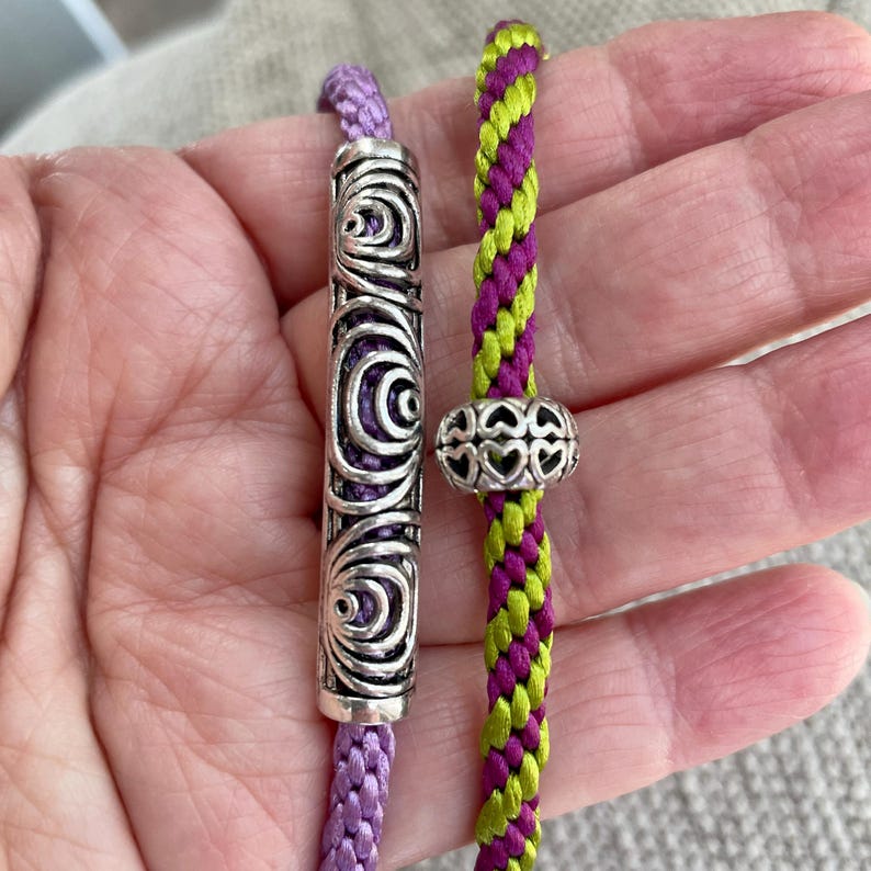 May include: Two braided cords with decorative metal beads. One cord is purple and the other is green and purple.