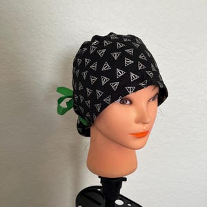 May include: Black surgical scrub cap with a white triangle pattern. The cap has a green ribbon tie in the back. The cap is displayed on a mannequin head.