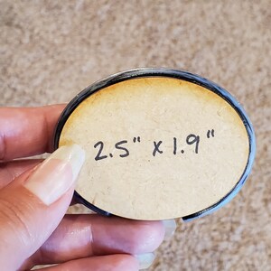 May include: A round, wooden coaster with a black border. The coaster has the text "2.5" x 1.9" written on it.