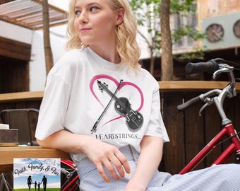 May include: White t-shirt with a pink heart and a black violin and bow graphic. The text "HEARTSTRINGS..." is below the graphic. The shirt is part of a clothing line.
