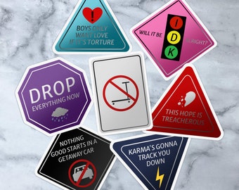 May include: Set of nine colorful stickers with various designs and text. The stickers feature a heart, a traffic light, a stop sign, a scooter, a broken heart, a car, a lightning bolt, and a rain cloud. The text on the stickers includes "Boys Only Want Love If It's Torture", "Will It Be Alright?", "Drop Everything Now", "Nothing Good Starts In A Getaway Car", "This Hope Is Treacherous", "Karma's Gonna Track You Down", and "Will It Be Alright?"