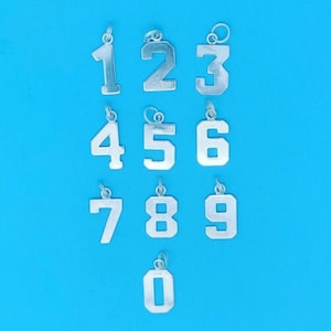 Puede incluir: Diez abalorios plateados en forma de números del 0 al 9. Los abalorios están sobre un fondo azul.
