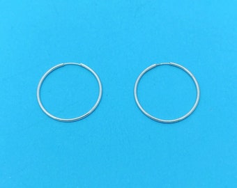 May include: A pair of silver hoop earrings on a blue background.